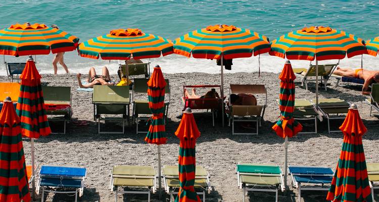 Bunte Sonnenschirme und Liegestühle an einem Sandstrand.
