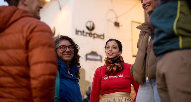 Un chef de groupe Intrepid discute avec des voyageurs devant un bâtiment colonial au crépuscule.