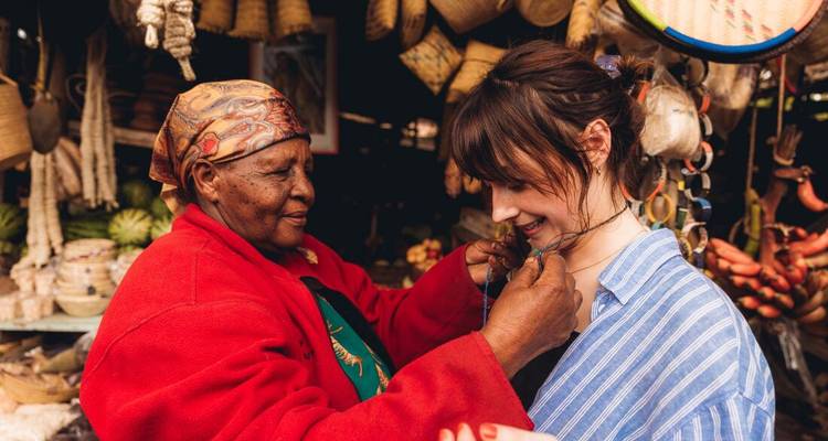 Femme âgée offrant un collier à une femme plus jeune dans un marché.