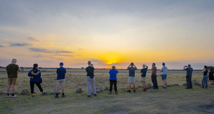 Personas observando una puesta de sol sobre un paisaje llano.