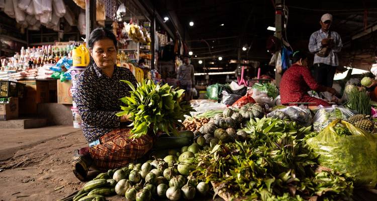 Femme triant des légumes frais dans un marché animé.