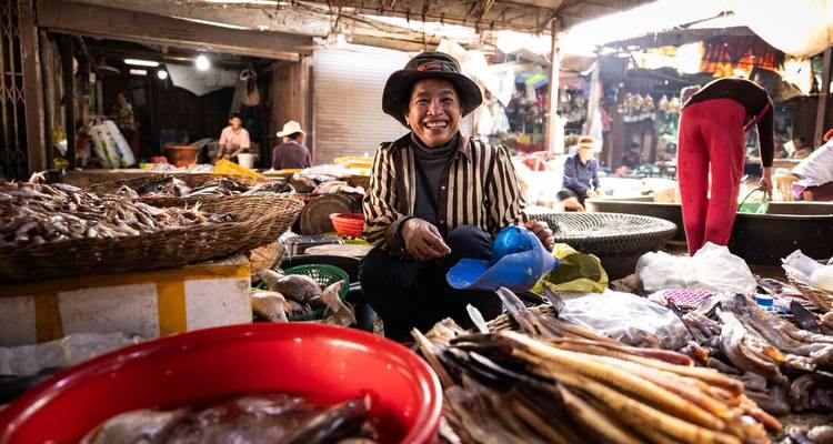 Une femme souriante entourée de poissons dans un marché animé.