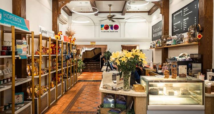 Un interior de boutique bien iluminado y café alineado con recuerdos, snacks y un mostrador de pastelería.