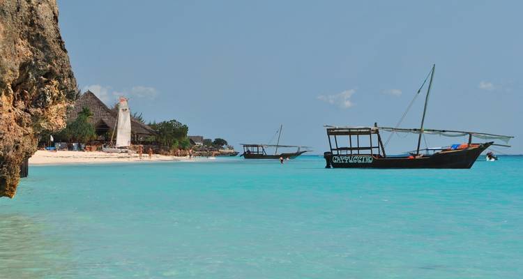 Strandgezicht met traditionele dhow-boten en helder turquoise water.