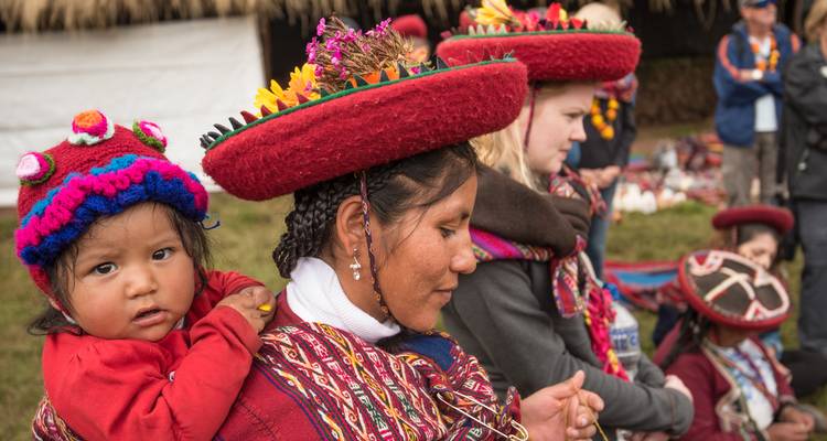 Indigene Frauen in bunter traditioneller Kleidung, eine trägt ein kleines Kind auf dem Rücken, nehmen an einer kulturellen Versammlung teil.