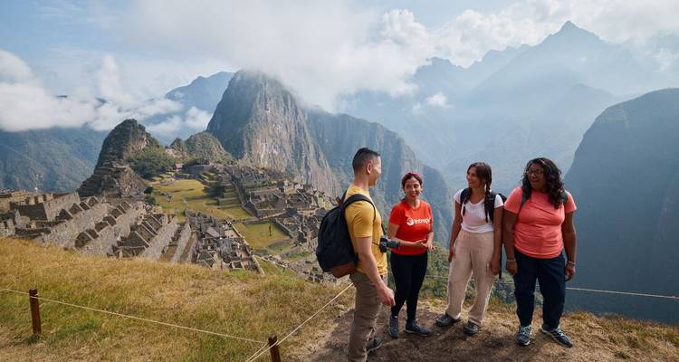 Petit groupe de voyageurs discutant avec un guide sur le belvédère du Machu Picchu avec les ruines incas en contrebas.
