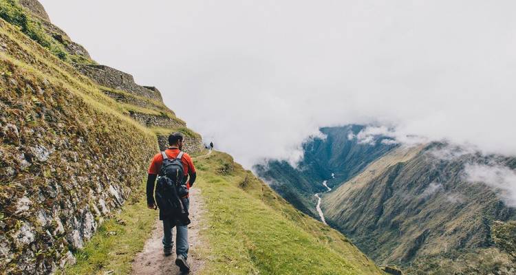 Randonneur solitaire marchant le long d'une section brumeuse du Chemin de l'Inca avec une vallée spectaculaire en contrebas.