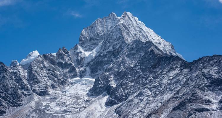 Dramatische sneeuwbedekte Himalayatop tegen een diepblauwe hemel, met scherpe bergkammen en gletsjers.