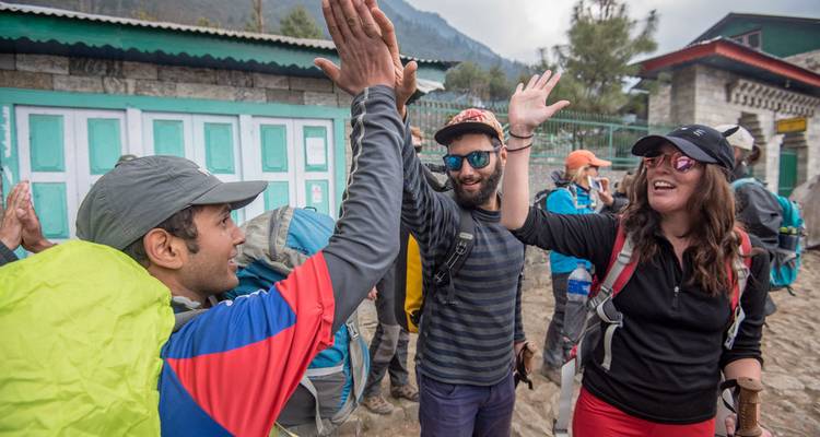 Blije trekkingstoeristjes geven elkaar high-fives buiten een Nepalees dorpslogies dat turquoise en wit is geschilderd.