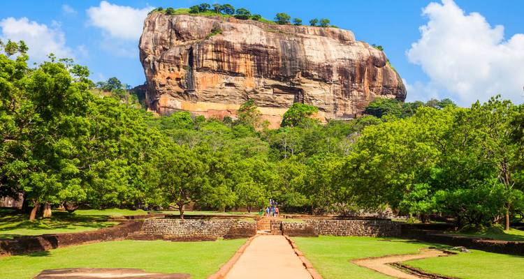 La forteresse rocheuse de Sigiriya encadrée par des jardins verdoyants et une allée centrale sous des nuages blancs et cotonneux.