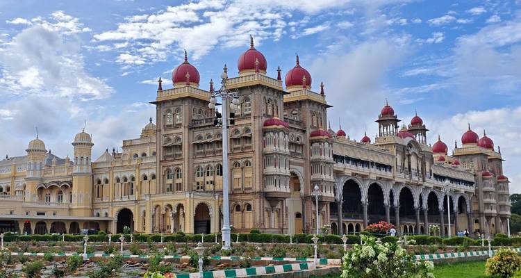 Das majestätische Mysore Palace mit seinen Kuppeltürmen und gepflegten Gärten unter blauem Himmel.