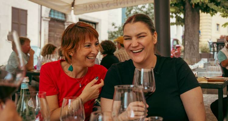 Des amis rient en buvant des verres de vin rouge dans une trattoria italienne en plein air.