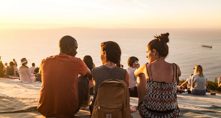 Grupo sentado en una colina costera viendo el atardecer.