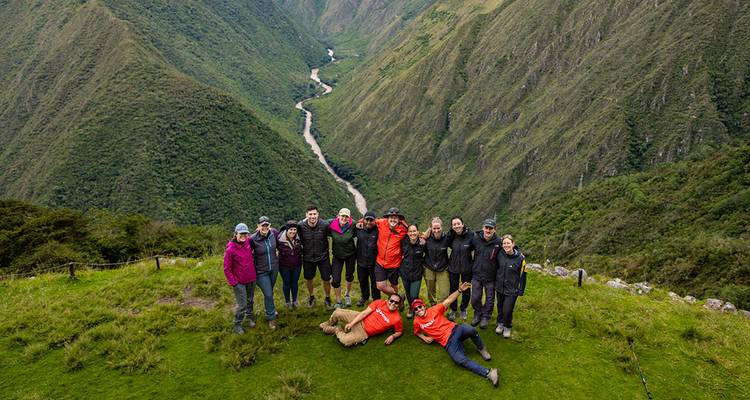 Een grote groep mensen die poseert voor een schilderachtig berglandschap met een rivier eronder.