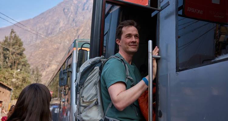 Een rugzakreiziger stapt in een blauwe treinwagon tegen de achtergrond van steile Andesbergen.