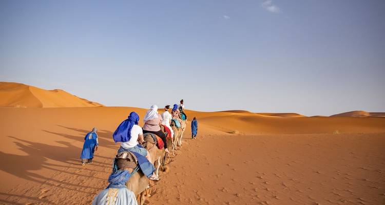 Caravana de turistas montando en camellos a través de enormes dunas de arena anaranjada