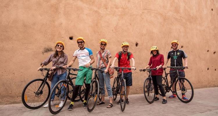 Ciclistas sonrientes posan con sus bicicletas contra una pared de tonos tierra usando cascos amarillos