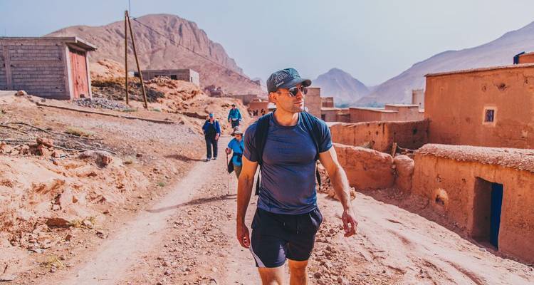 Hombre caminando por un sendero polvoriento del pueblo de montaña con picos áridos de fondo