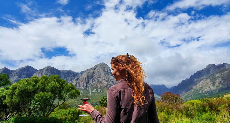 Femme aux cheveux roux tenant un verre de vin, montagnes en arrière-plan.