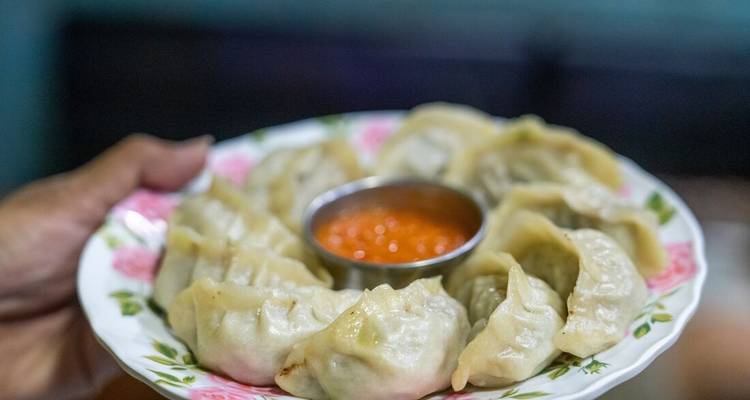 Plato de momos nepalíes al vapor arreglados en un anillo alrededor de una salsa picante para acompañar.
