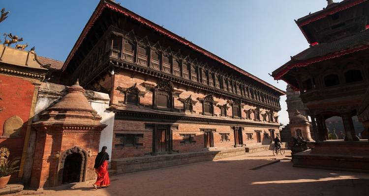 Escena de madrugada del complejo palaciego de ladrillos rojos de Bhaktapur con una mujer vestida tradicionalmente caminando sola.
