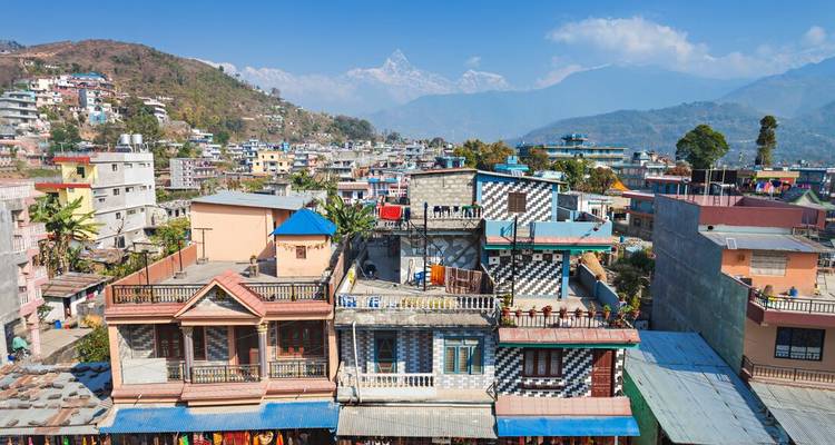 Panorámica del skyline de Pokhara con edificios coloridos y el Himalaya nevado de fondo.
