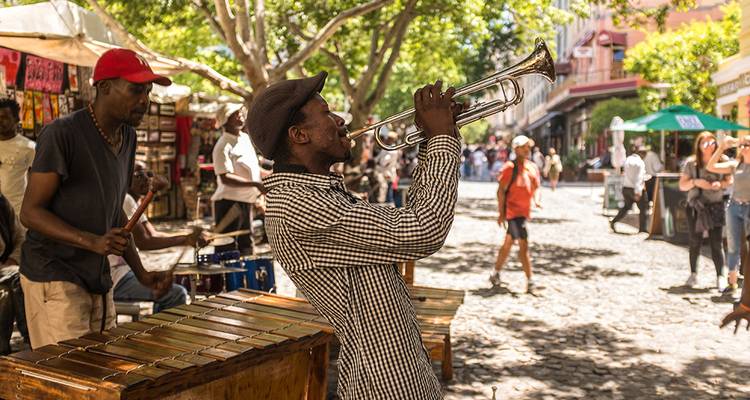 Músicos callejeros tocando instrumentos con un fondo vibrante de un mercado al aire libre.