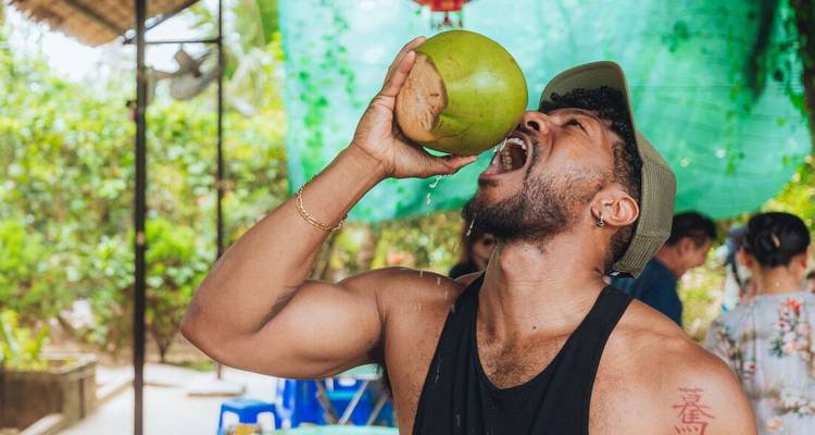 Voyageur buvant avec enthousiasme une noix de coco fraîche à un étal rural vietnamien