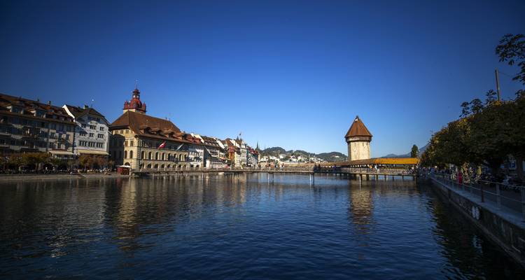 Le pont de la Chapelle en bois de Lucerne et la tour octogonale de l'eau s'étendent au-dessus de la paisible rivière Reuss sous un ciel bleu clair.