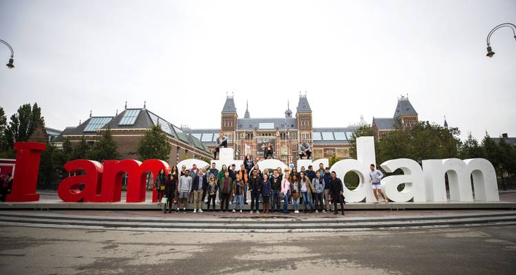 Un grand groupe de voyageurs pose sur les célèbres lettres rouge et blanc 'I amsterdam' devant le Rijksmuseum.