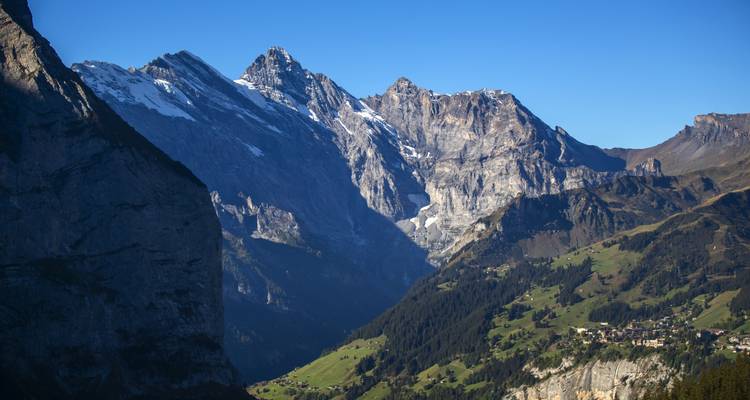 Des pics rocheux imposants projettent leurs ombres sur une vallée verdoyante parsemée de petits villages alpins.