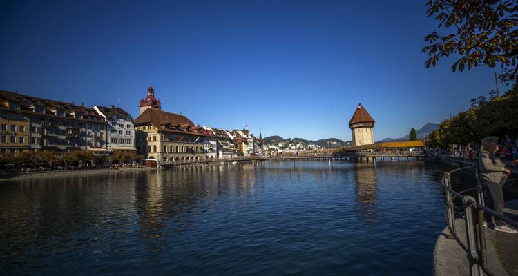 Historic buildings alongside a calm river with reflections.
