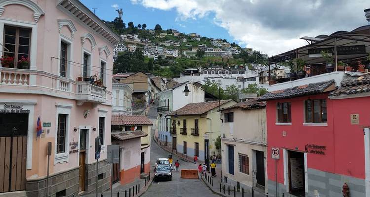 Des maisons coloniales colorées bordent une rue pavée escarpée à Quito, avec la statue de la Vierge surplombant la ville.