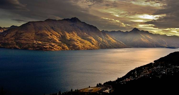 La puesta de sol dorada lanza una luz cálida sobre el lago oscuro y las escarpadas cimas de las montañas