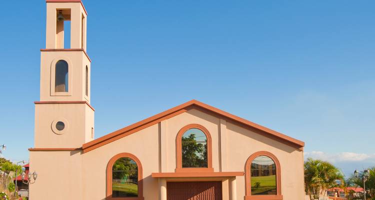 Pequeña iglesia beige con campanario recortada contra un cielo azul despejado