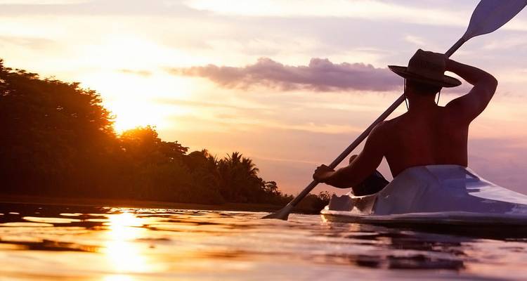 El kayakista rema a través del agua tranquila al atardecer con reflejos dorados