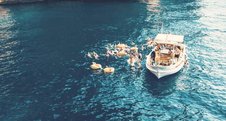 Bateau de fête ancré dans une eau bleu profond tandis que des nageurs flottent autour sur des bouées gonflables.