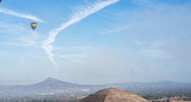 Une montgolfière dérive au-dessus de la Pyramide du Soleil à Teotihuacan avec des montagnes brumeuses en arrière-plan.
