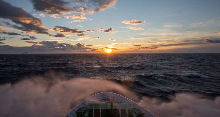 Coucher de soleil sur les mers agitées de l'Antarctique alors que des embruns s'élèvent de la proue du navire