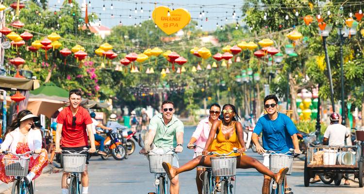 Los amigos montan bicicletas alegremente bajo faroles coloridos en una calle animada de Hoi An.