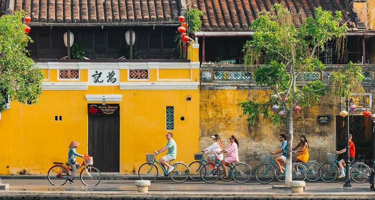 Des cyclistes longent un mur colonial jaune orné de lanternes dans la vieille ville de Hoi An.
