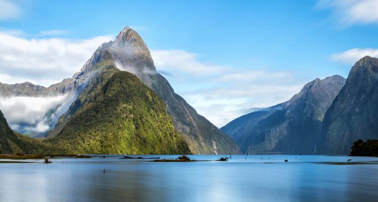 Le pic Mitre emblématique s'élevant abruptement des eaux calmes et réfléchissantes du Milford Sound sous un ciel bleu éclatant.