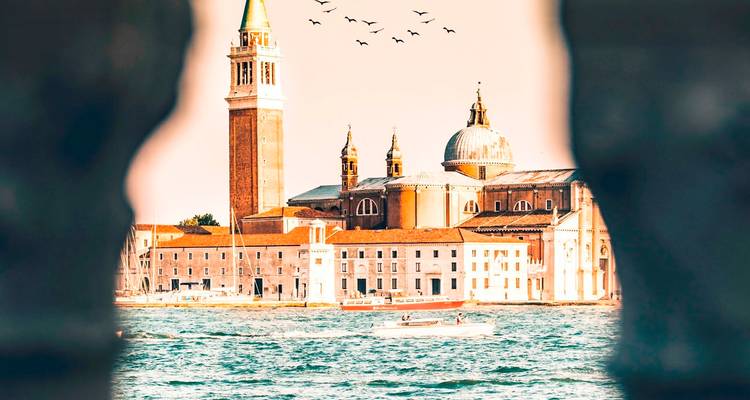 A view of Venice with San Giorgio Maggiore seen through a stone frame, with birds in the sky.
