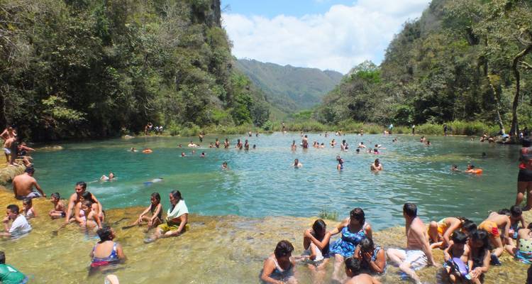 People swimming and relaxing in a natural water pool surrounded by mountains.