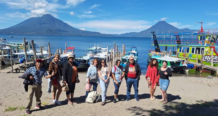 Groupe debout près de bateaux sur une rive avec des volcans en arrière-plan au Guatemala.