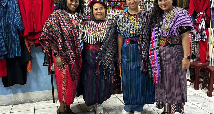 Femmes en tenue traditionnelle posant devant des tissus colorés au Guatemala.