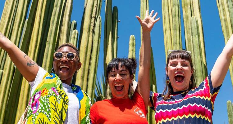 Three women posing excitedly in front of tall cacti.
