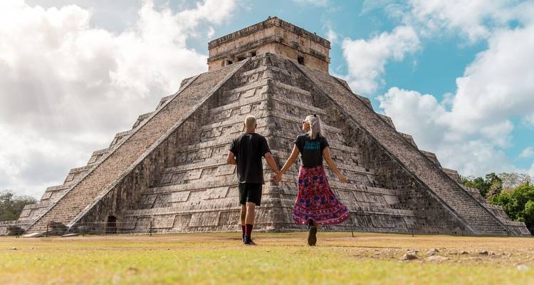 Couple holding hands facing an ancient stepped pyramid.