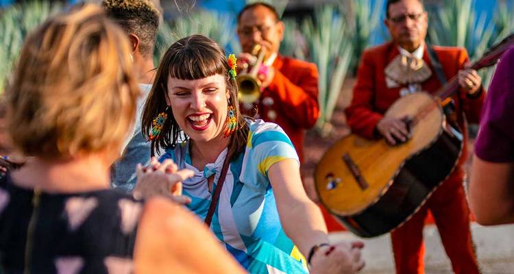 A group of people dancing with joyful expressions, musicians in the background.