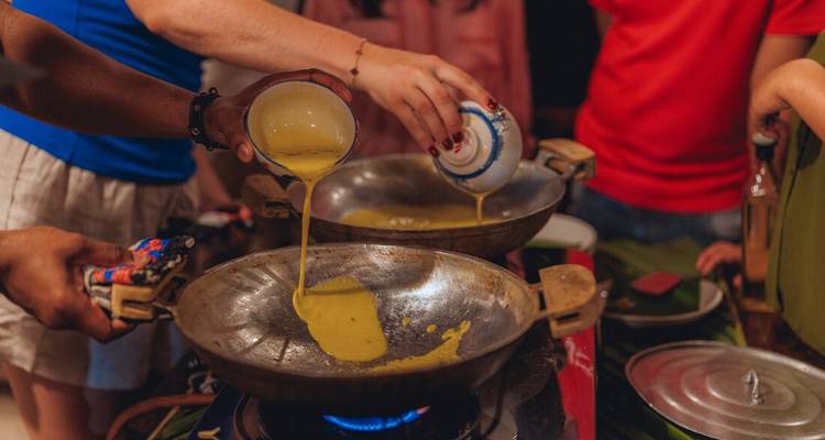 Las manos vierten masa en woks calientes sobre llamas de gas durante una sesión de cocina interactiva